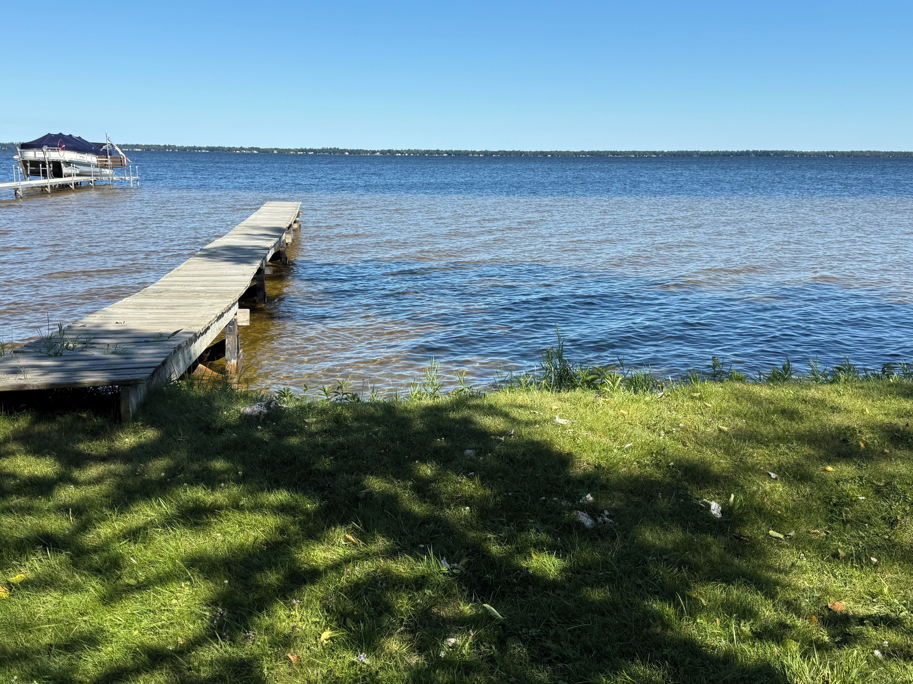 A wooden dock extending into a calm lake with a grassy area in the foreground.