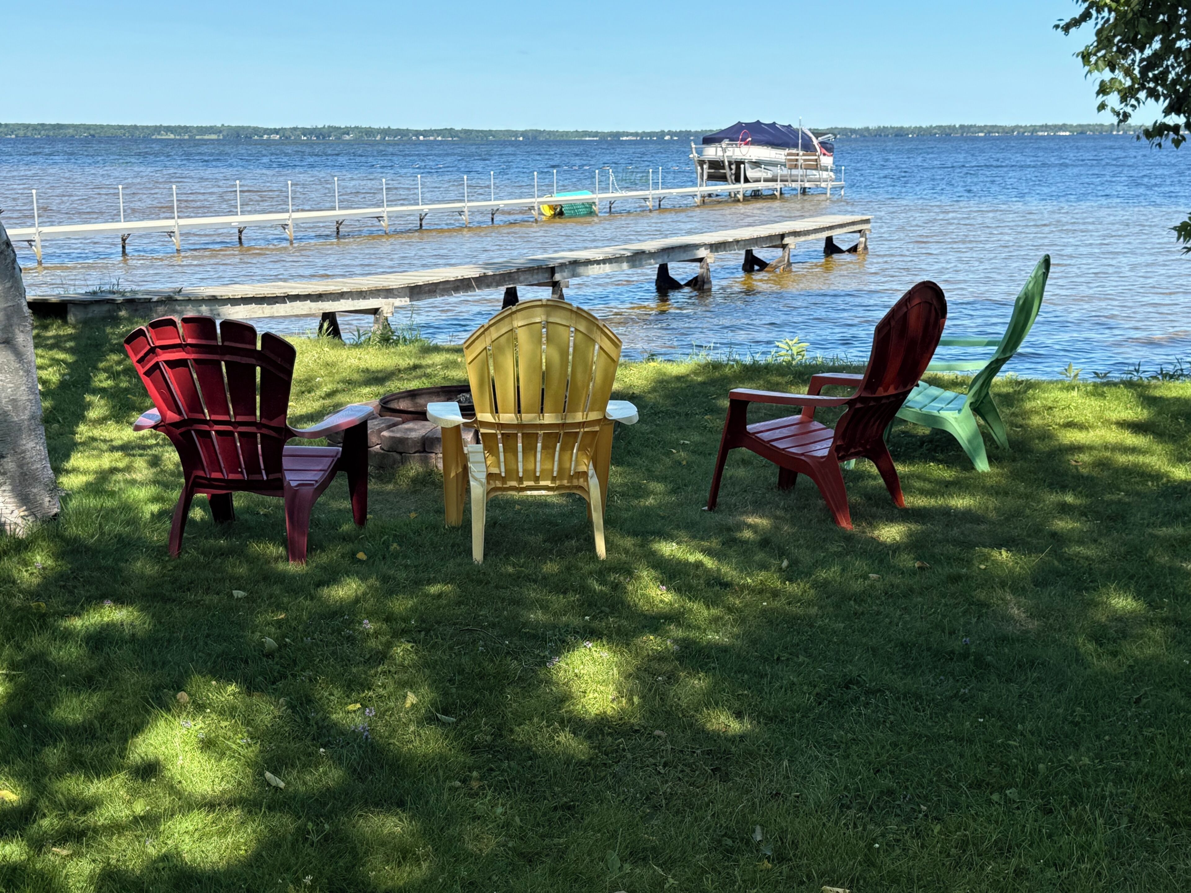 Un área de estar junto al lago con sillas Adirondack y un muelle que se adentra en el agua.