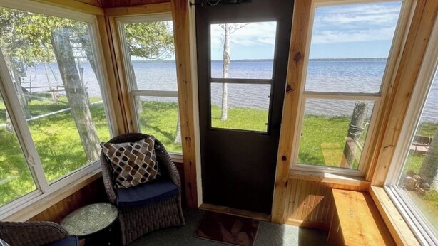 Un chalet confortable avec un intérieur en bois, de grandes fenêtres donnant sur un lac et un petit coin salon avec un fauteuil et des coussins.