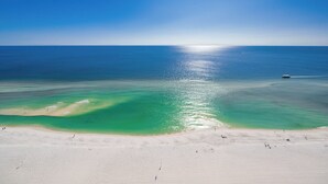 Une plage aux eaux turquoise et limpides, un rivage sablonneux et un bateau à l’horizon.