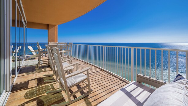 Un balcon donnant sur l’océan, des chaises en bois et une balustrade blanche.
