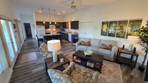 A spacious living room with a sofa, armchairs, and a coffee table. A kitchen is visible in the background with a dining area.
