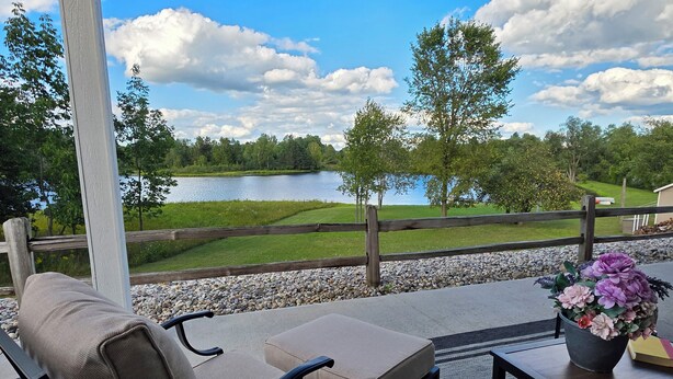 A covered outdoor seating area with a view of a lake, a wooden fence, and a garden with flowers.