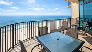 A balcony with a glass table and chairs, overlooking a beach and the ocean. - Spacious Beachfront Comfort  Phoenix West 1005 (Orange Beach)