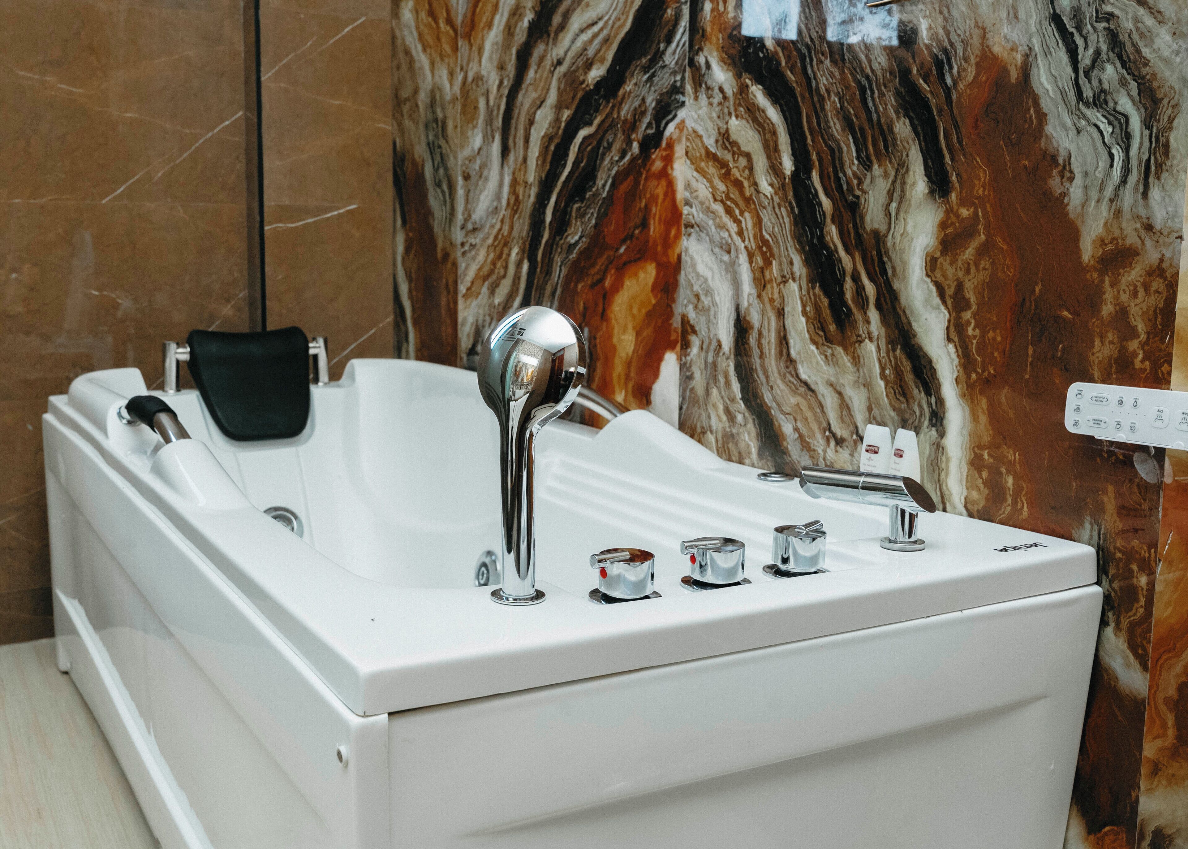 A modern bathroom with a freestanding bathtub, a handheld showerhead, and a wall-mounted control panel.