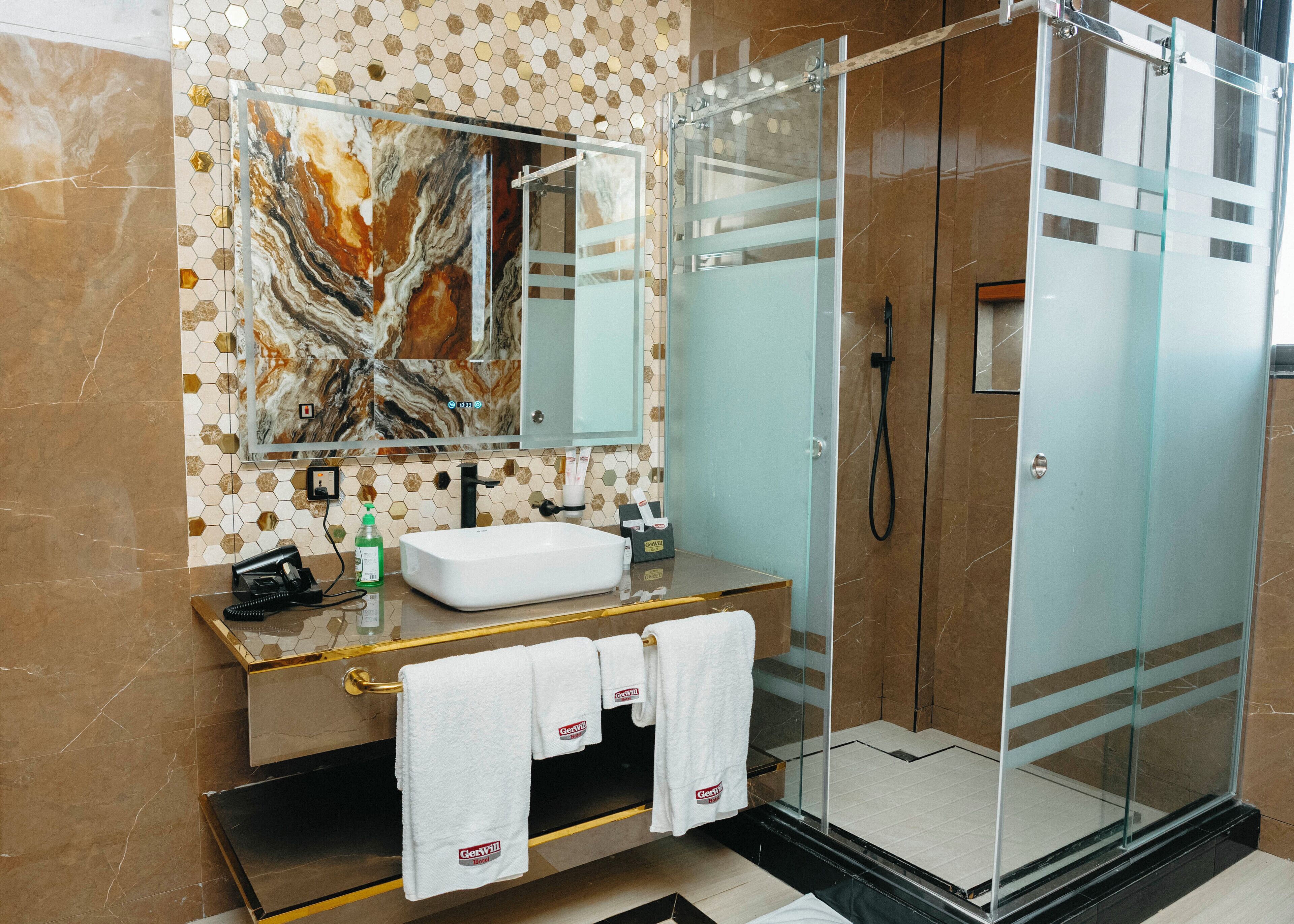 A modern bathroom with a glass-enclosed shower, a marble-tiled vanity, and a large mirror.
