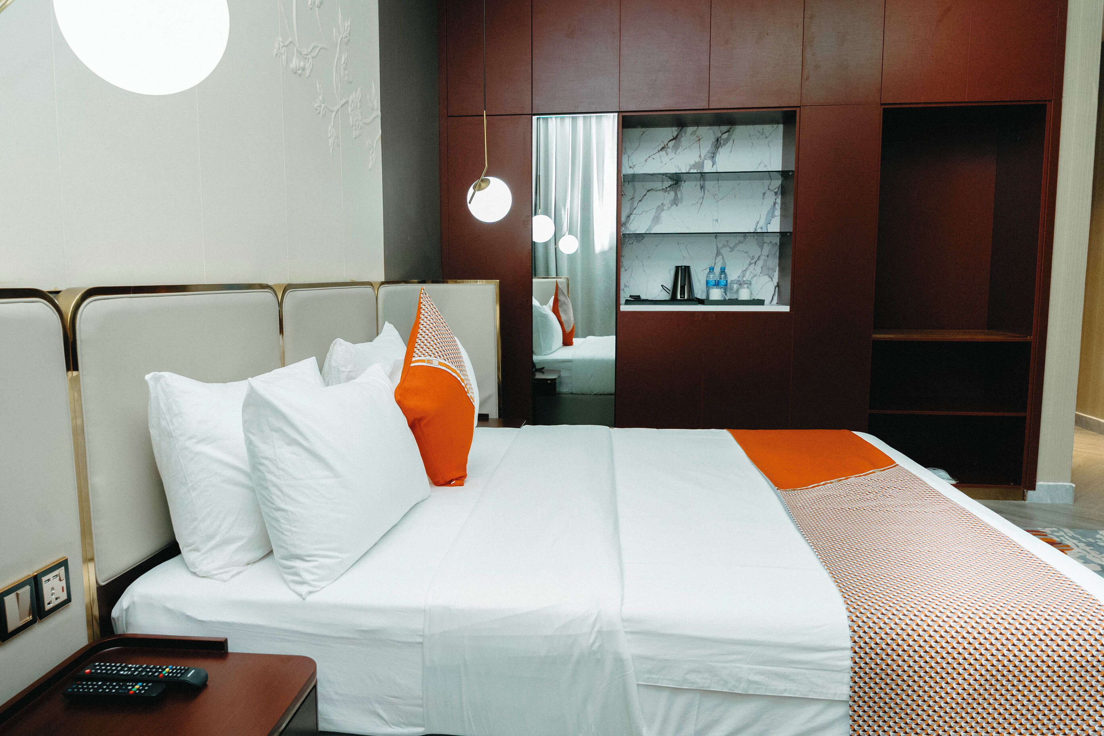A hotel room with a bed, a nightstand, a mirror, a shelf with toiletries, and a wall with a circular design.