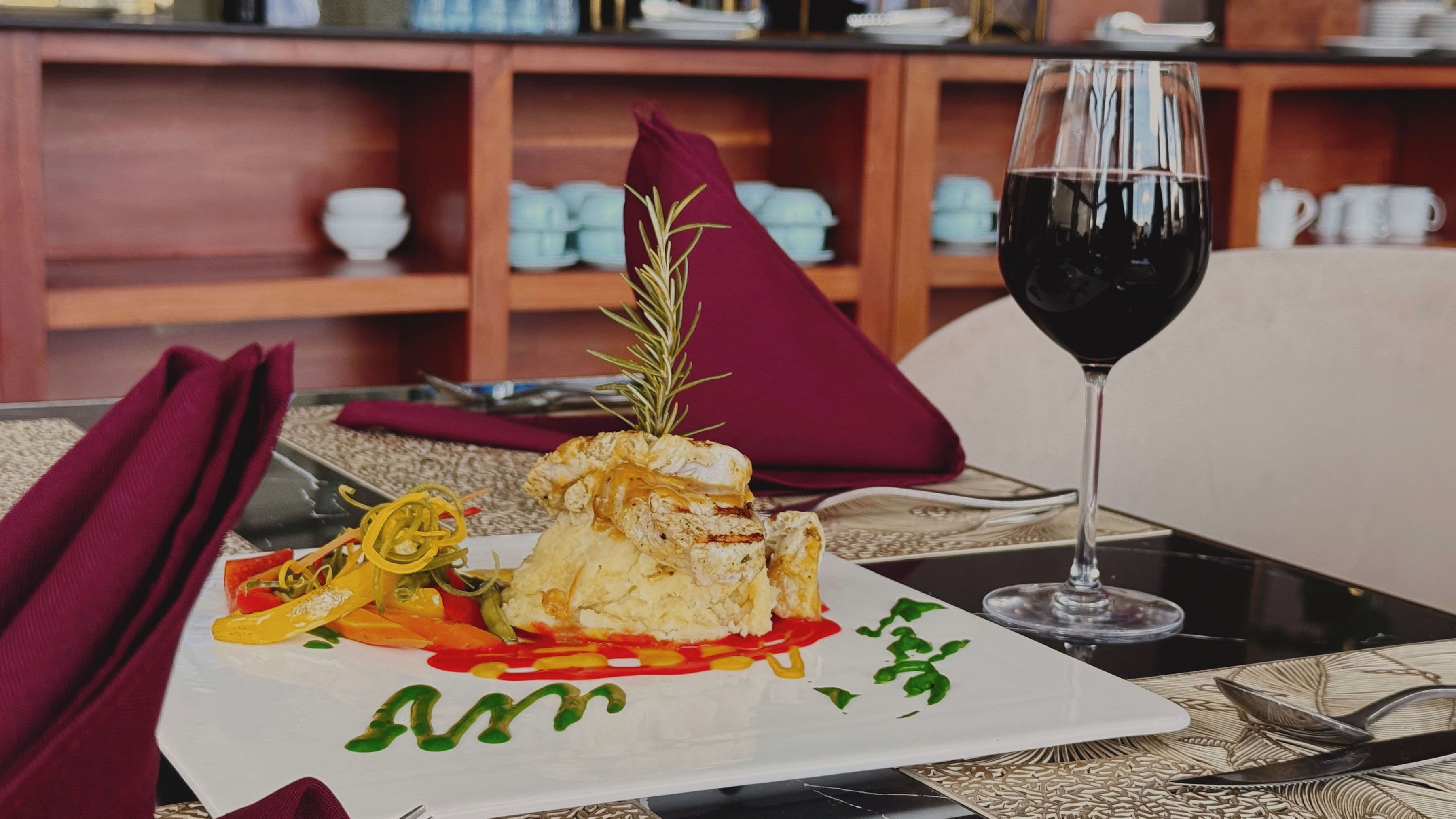 Une table à manger avec une assiette de nourriture, un verre de vin rouge et une serviette.