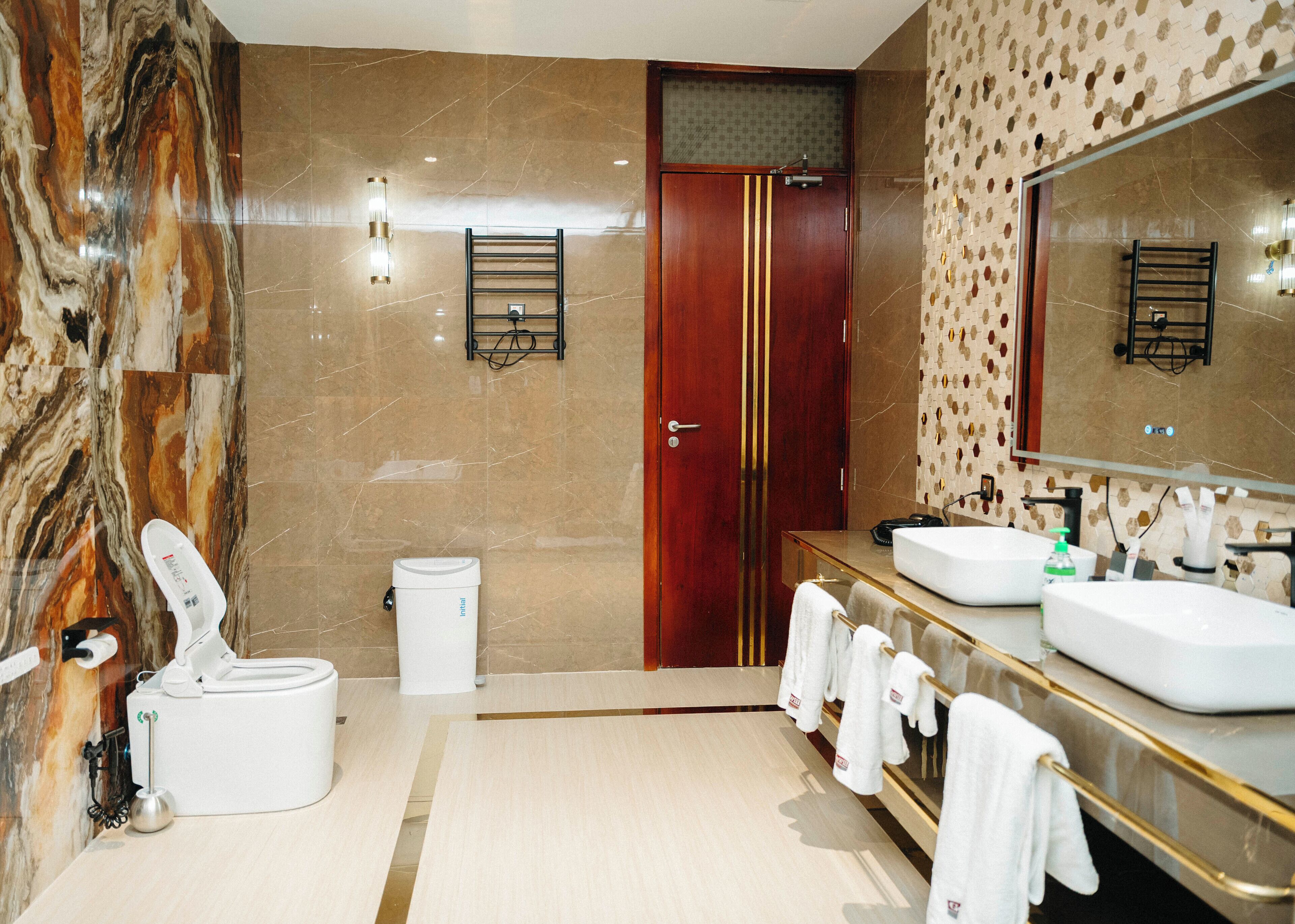 Un baño moderno con paredes de mármol, una puerta de madera, un espejo grande y dos lavamanos.