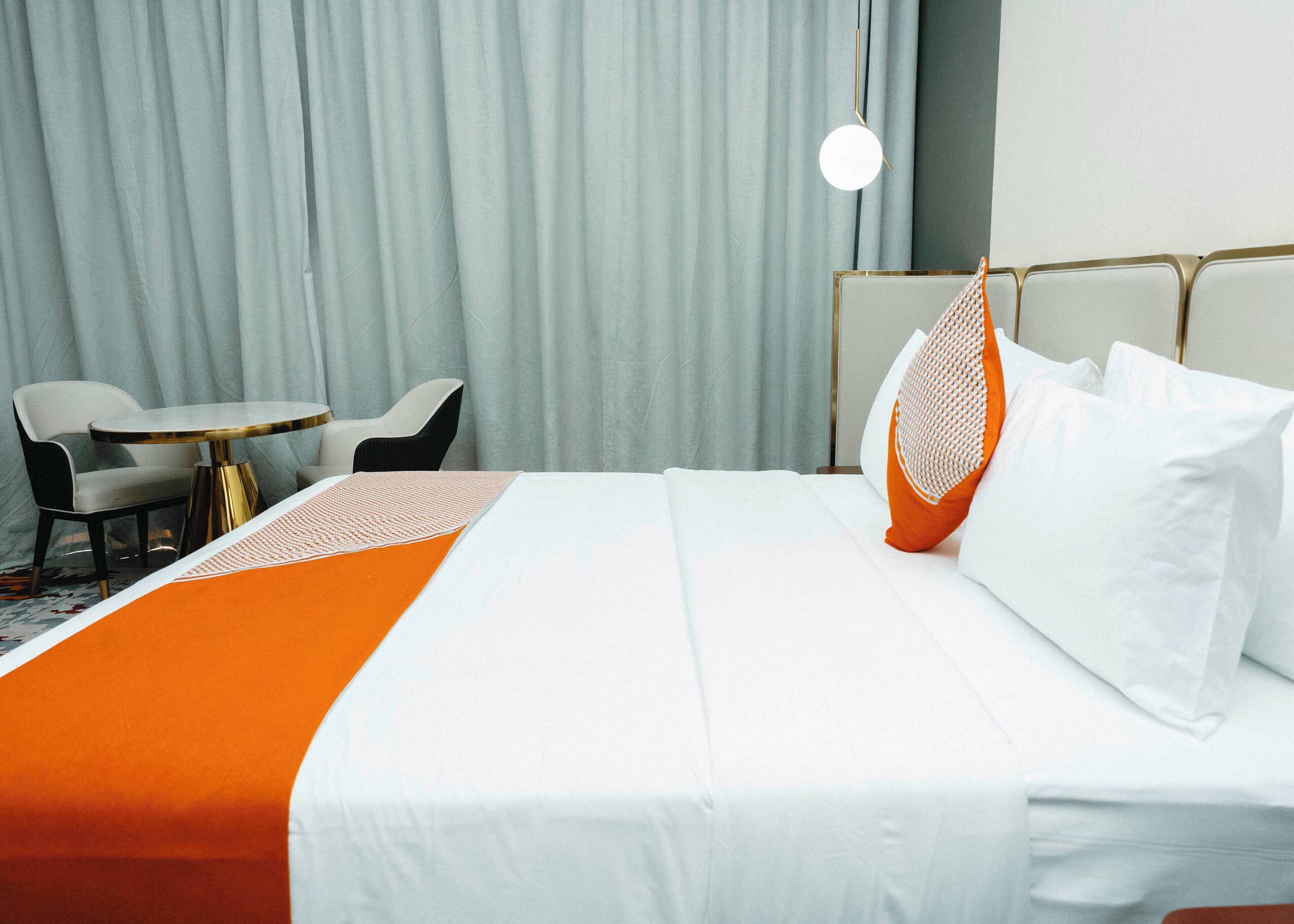A hotel room with a bed, two chairs, a small round table, and a hanging light fixture.
