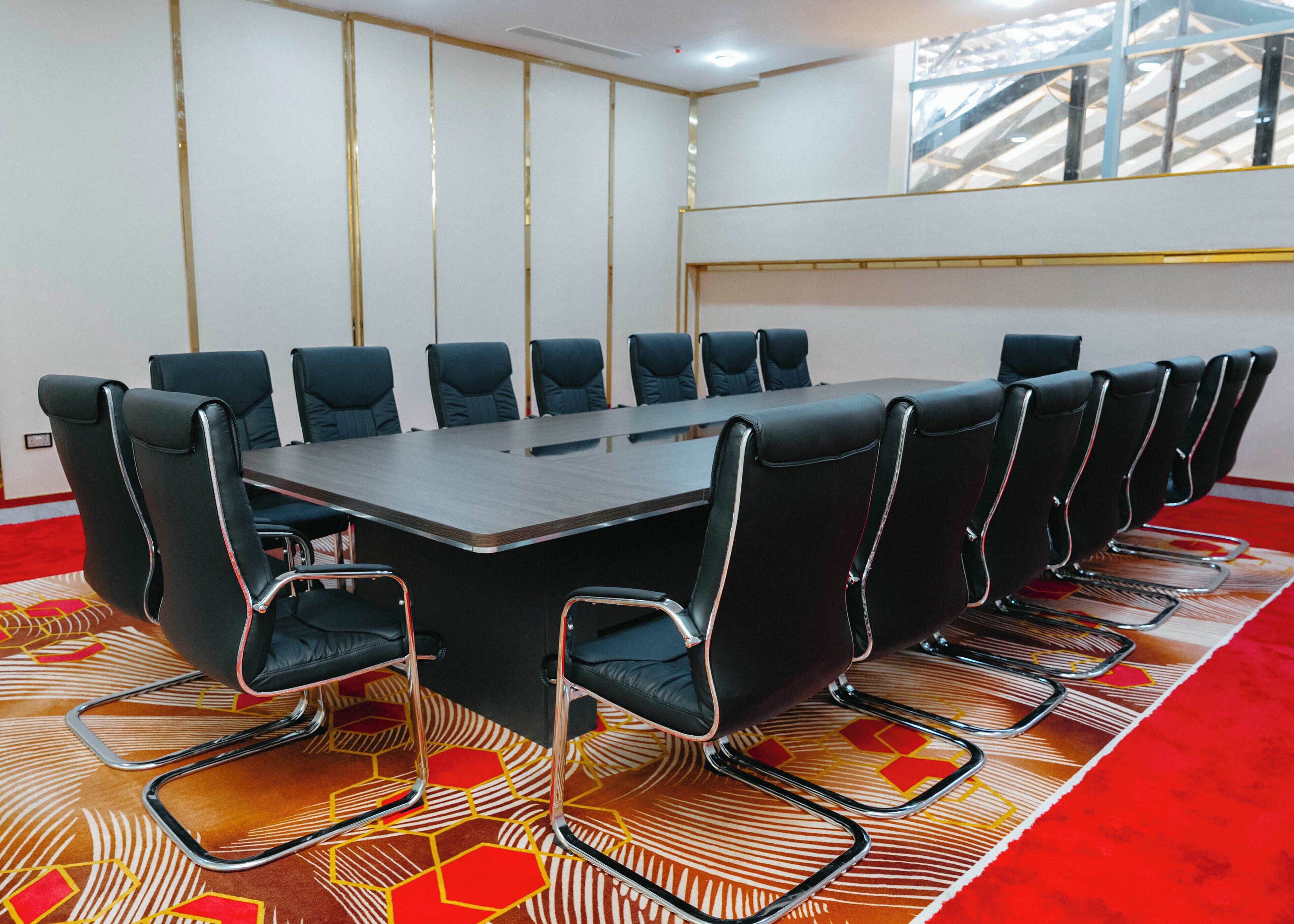 A conference room with a long table and 12 chairs, a patterned carpet, and a staircase in the background.