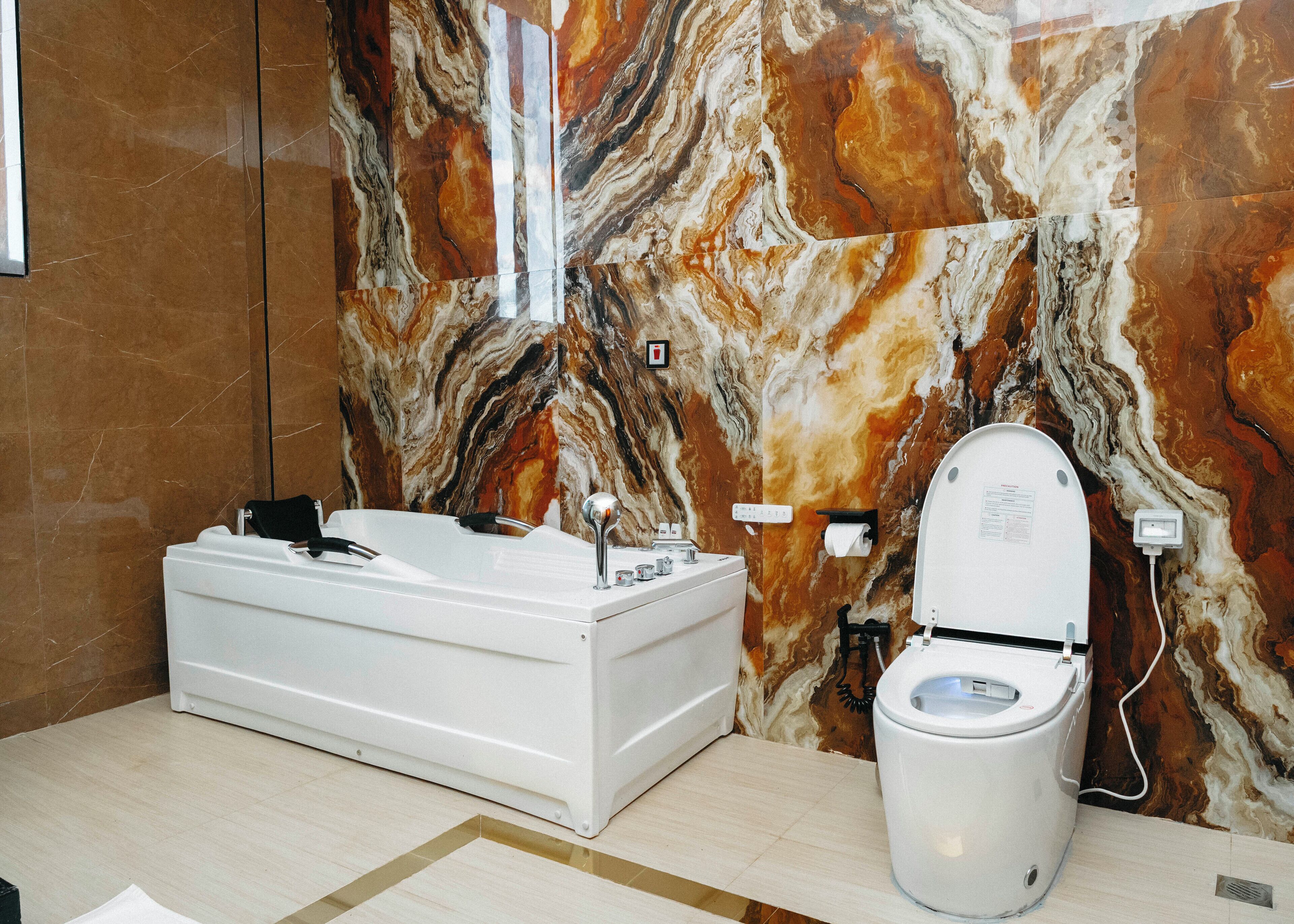 A bathroom with a marble wall, a white bathtub, and a toilet.