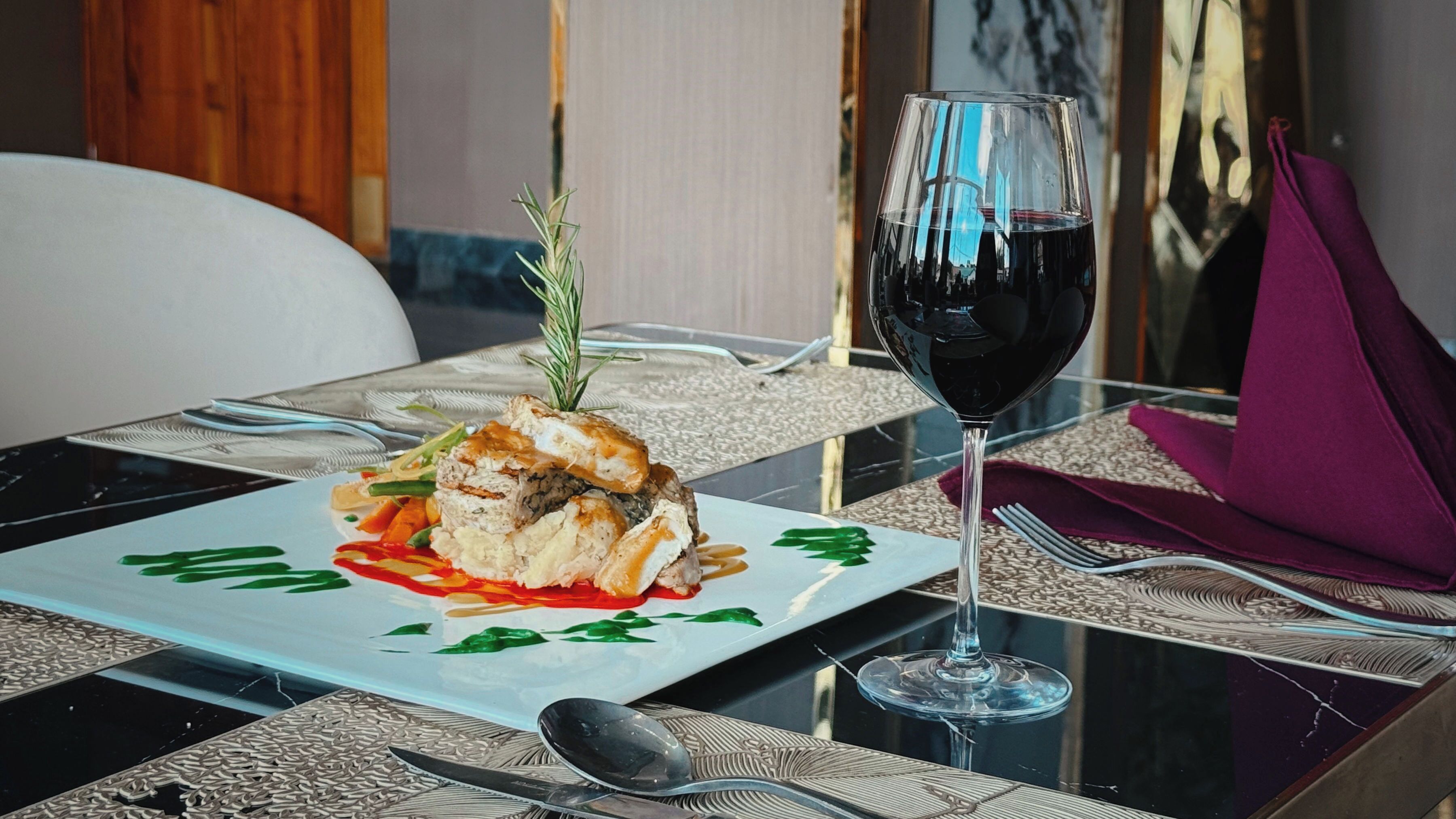 A dining table with a plate of food, a glass of red wine, and cutlery.