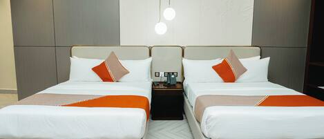 Habitación doble con dos camas, cada una con ropa de cama blanca y detalles en naranja, una mesita de noche pequeña con teléfono y una lámpara de pared.