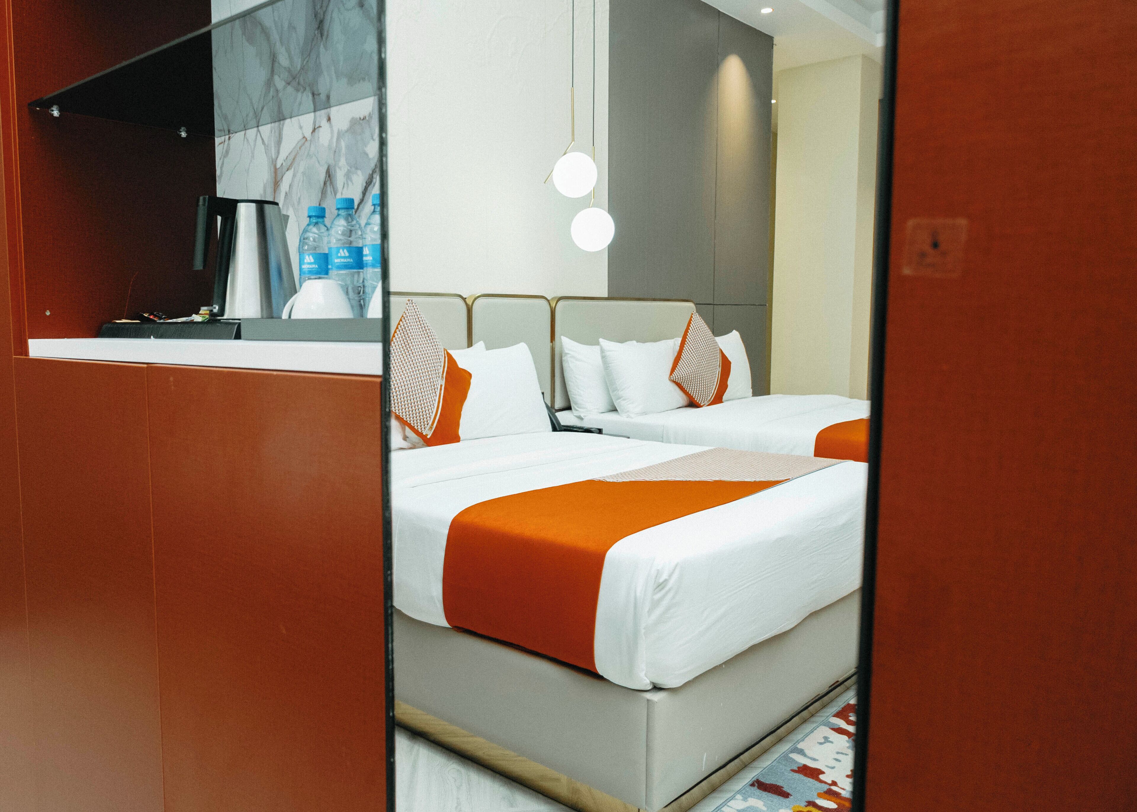 A hotel room with two beds, a large mirror, and a minibar.