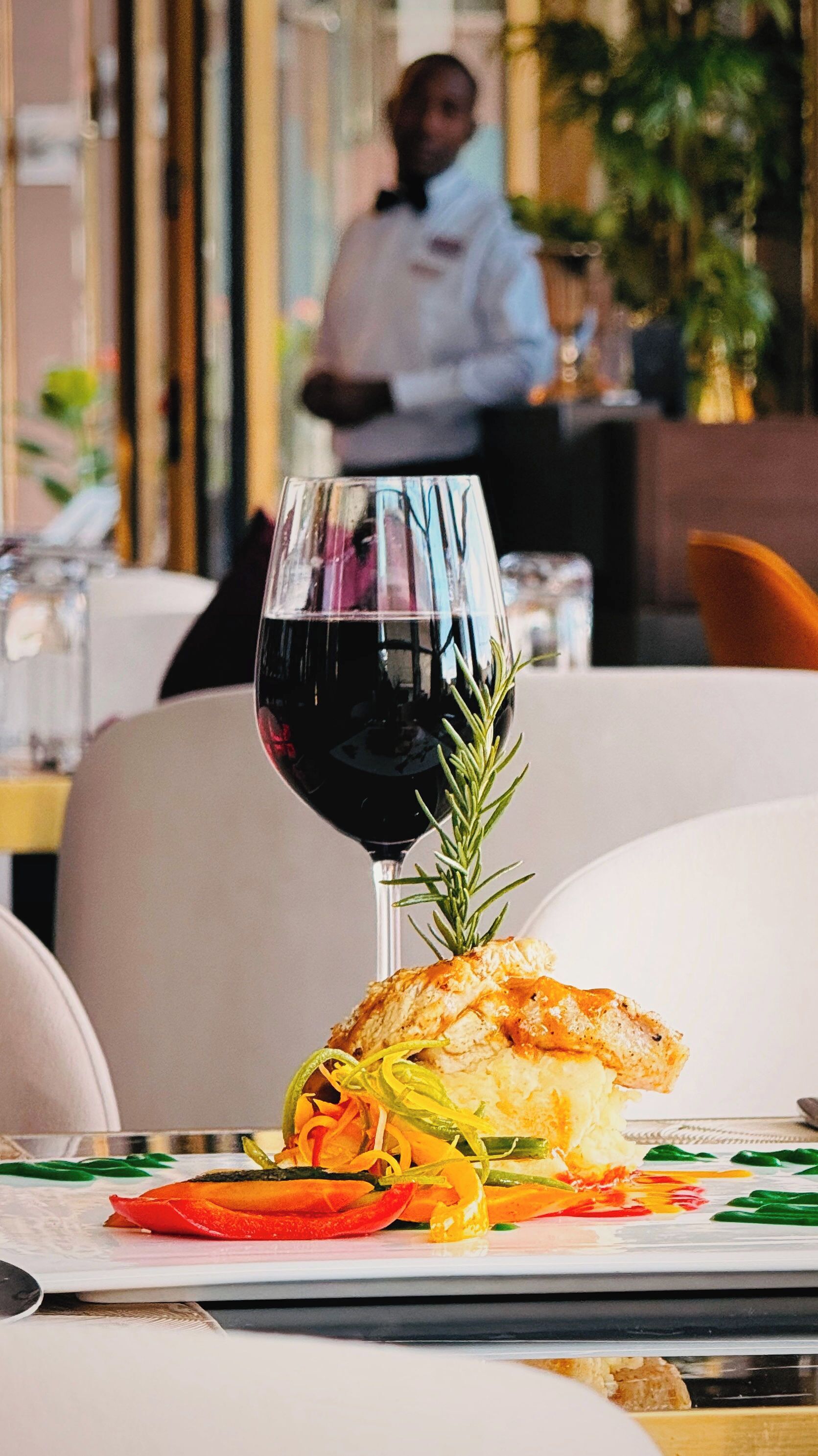 Una mesa de comedor con un plato de comida, una copa de vino tinto y una ramita de romero.