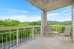 A balcony with a concrete pillar, white railing, and two wicker chairs.