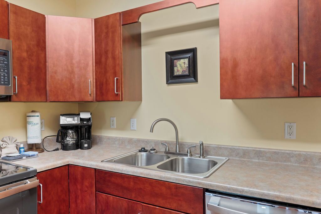 A kitchen with stainless steel sinks, a coffee maker, and wooden cabinets.