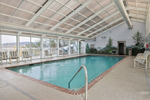 An indoor swimming pool with a covered roof, clear glass walls, and a view of the outdoors.
