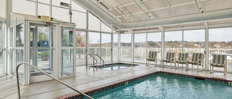 Una piscina interior con paredes de vidrio transparente, una zona techada con sillas y una señal de salida.