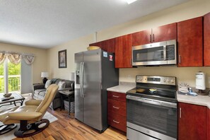 A compact kitchen with a refrigerator, microwave, oven, and wooden cabinets.