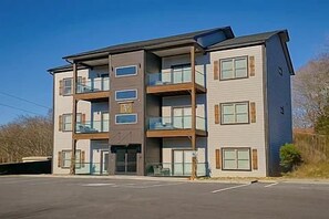 A multi-story building with balconies, a parking lot, and a clear sky.