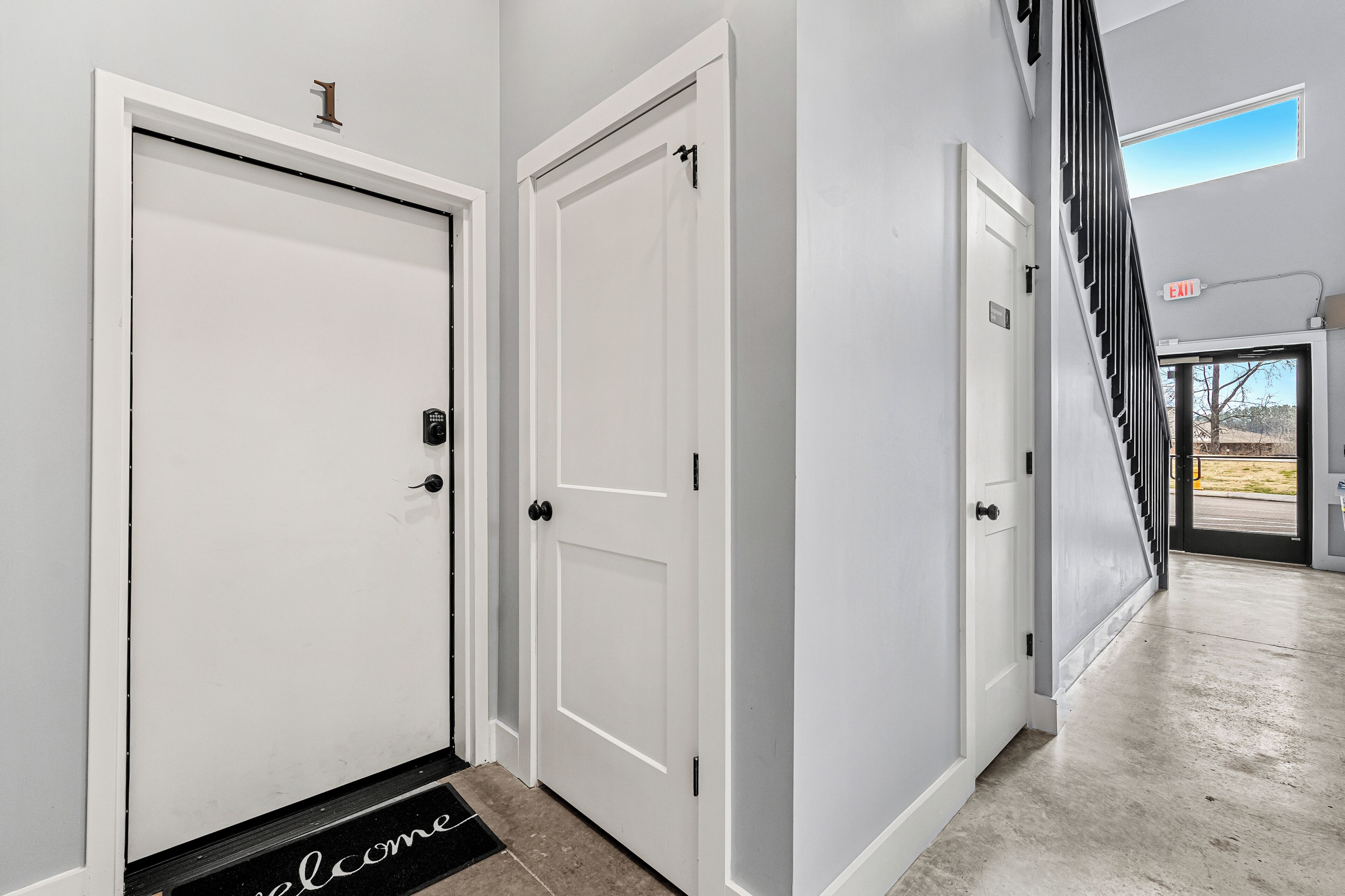 A hallway with white doors, a welcome mat, and an exit sign.