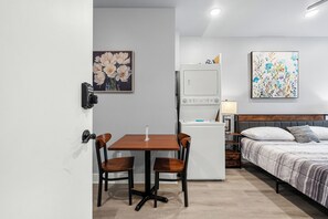 Ein kleines Hotelzimmer mit einem Bett, einem Schreibtisch mit zwei Stühlen, einem Kühlschrank und Bildern an den Wänden.