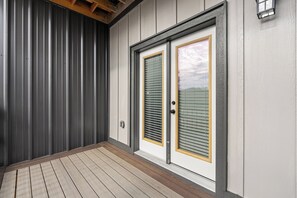 A wooden deck leading to a double door with a window, a metal wall, and a small wall-mounted light fixture. - Cozy Studio for 2 | Minutes from Dollywood in Sevierville (Sevierville)