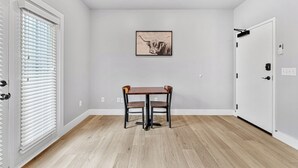 A room with a wooden floor, a table with two chairs, a door with a handle, and a wall-mounted light fixture. - Cozy Studio for 2 | Minutes from Dollywood in Sevierville (Sevierville)