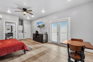A room with a bed, a desk, a chair, a ceiling fan, a TV mounted on the wall, and a sliding door with blinds. - Cozy Studio for 2 | Minutes from Dollywood in Sevierville (Sevierville)