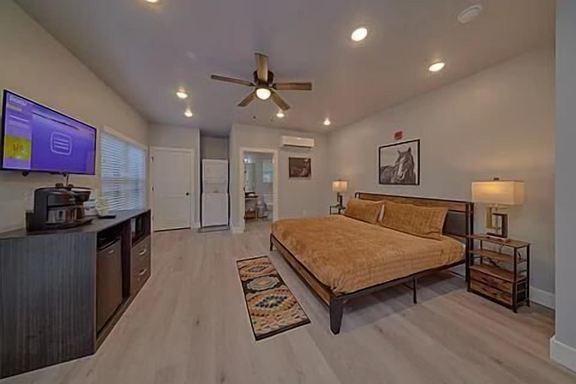A bedroom with a bed, bedside tables, a ceiling fan, a television, and a desk.