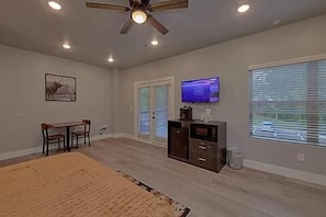 Ein Zimmer mit Deckenventilator, Fernseher, Essbereich und einem Fenster mit Jalousien.