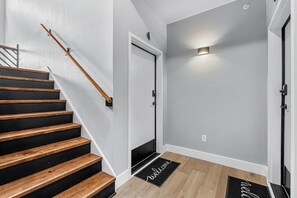 Un escalier avec des marches en bois et une rampe, menant à une porte au-dessus de laquelle se trouve un luminaire.