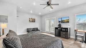 Une chambre moderne comprenant un lit, un bureau, une chaise, un ventilateur de plafond et une grande fenêtre avec des stores.