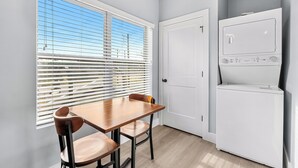 Une cuisine compacte comprenant une table et des chaises, un réfrigérateur blanc et une fenêtre avec des stores.