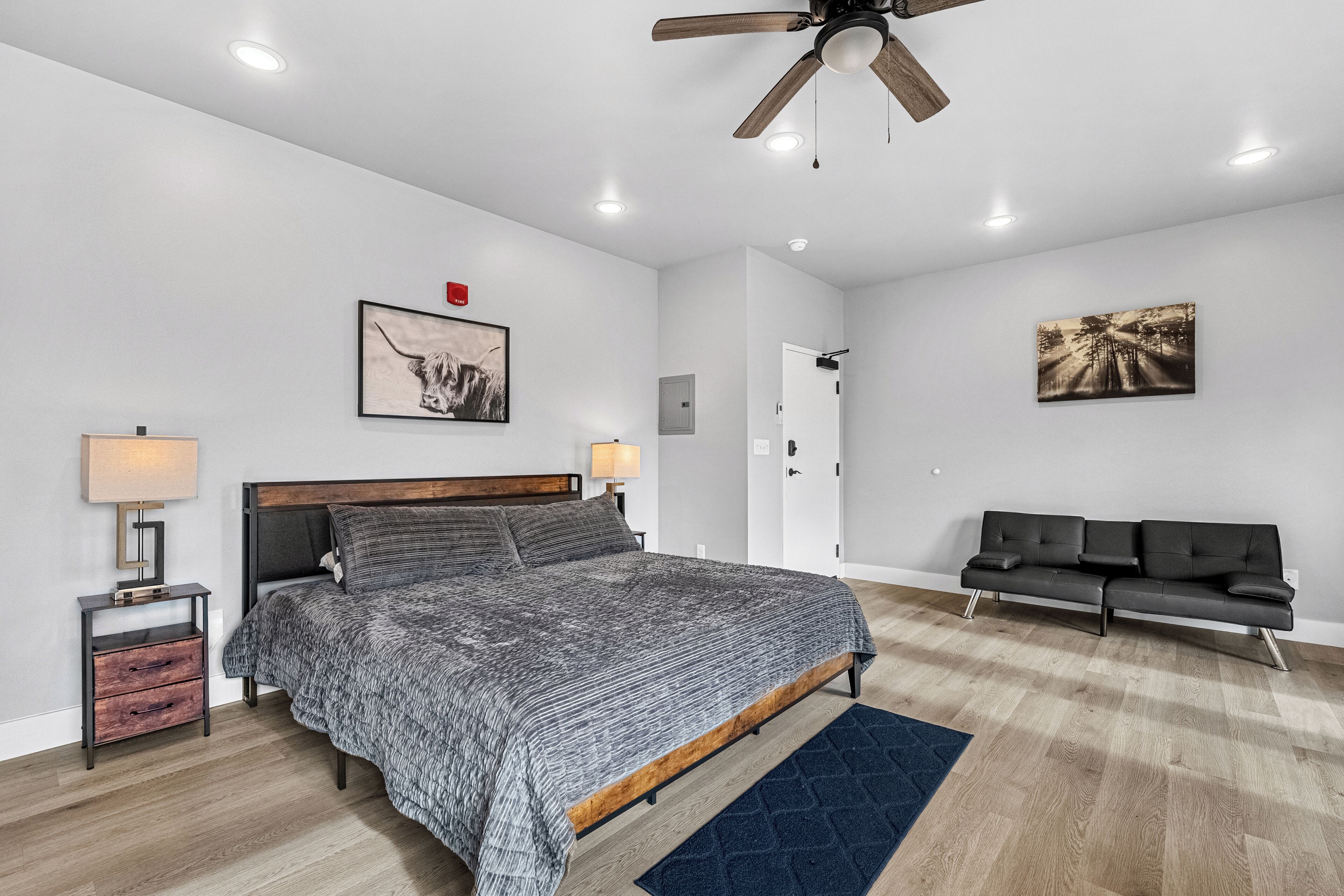 Une chambre à coucher moderne, avec un lit, des tables de chevet, un ventilateur de plafond et des œuvres d’art accrochées aux murs.