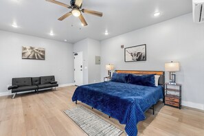 A bedroom with a bed, a black sofa, a ceiling fan, and two wall-mounted lamps.