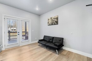 A modern living room with a black leather sofa, a painting on the wall, and a sliding glass door leading to an outdoor area.