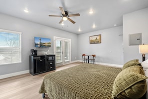 Une chambre à coucher comprenant un lit, un bureau, une chaise, un ventilateur de plafond et une fenêtre avec des stores.