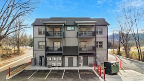 A multi-story residential building with a central entrance, air conditioning units, and a parking area.