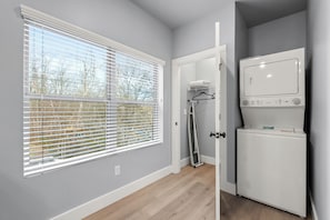 A laundry room with a washing machine, a drying rack, and a window with blinds.