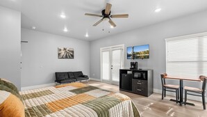 A modern bedroom with a bed, a sofa, a desk with a chair, a ceiling fan, and a television. - Studio Condo in Sevierville| King Bed| Sleeps 2 + Dollywood Ticket (Sevierville)
