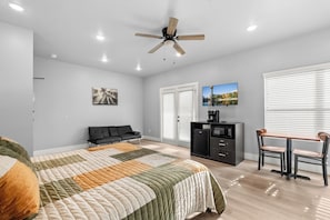 Une chambre moderne comprenant un lit, un canapé, un bureau avec une chaise, un ventilateur de plafond et un téléviseur.