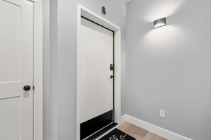 Un couloir avec une porte blanche, une porte noire et un luminaire fixé au mur.