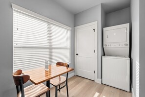 A compact kitchen with a wooden table, two chairs, a white refrigerator, and a closed door.