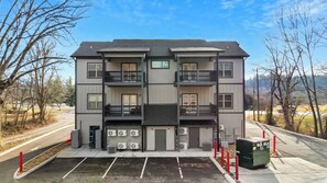 A multi-story residential building with a central entrance, air conditioning units, and a parking area.