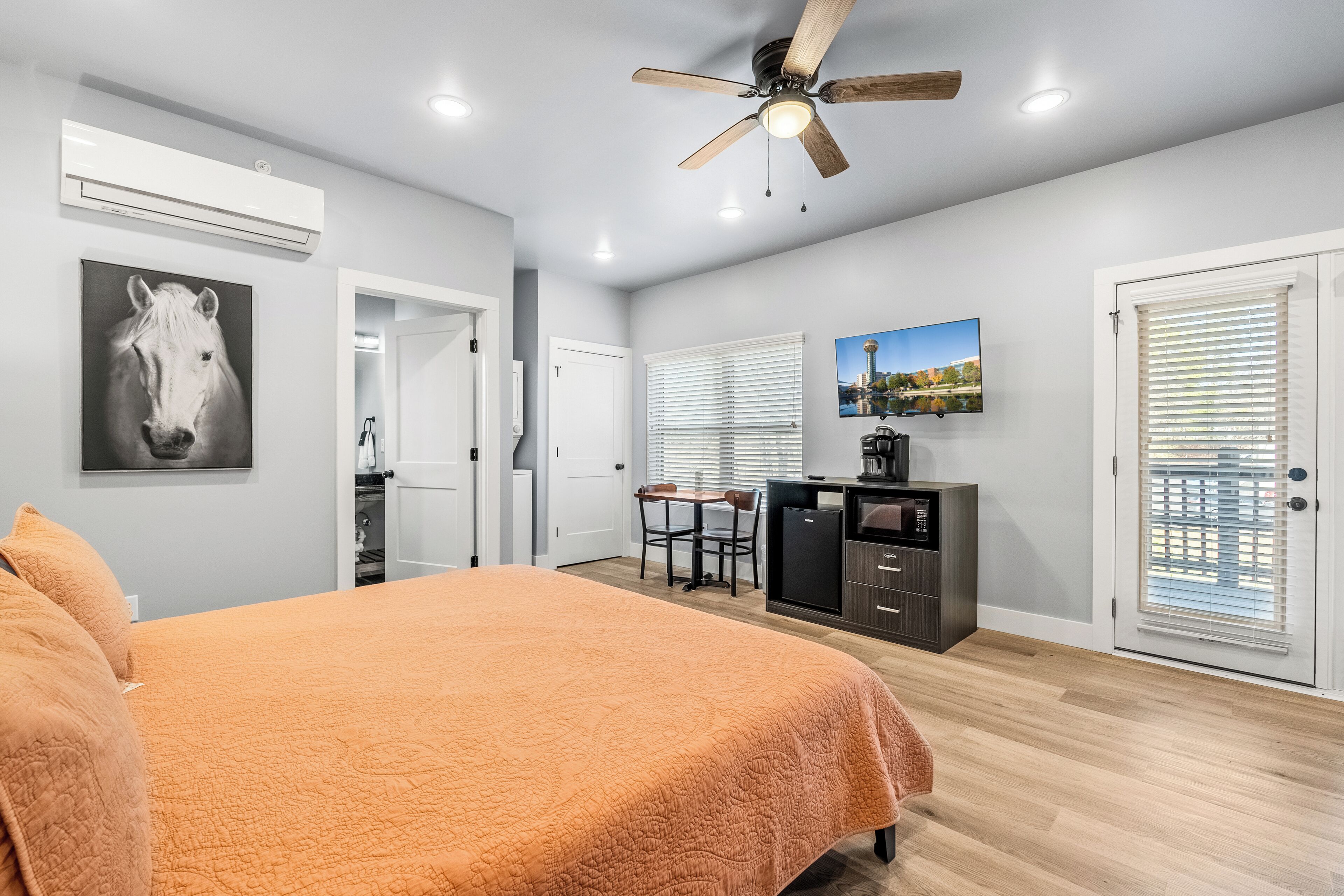 A bedroom with a bed, a ceiling fan, a desk with a chair, a television, and a refrigerator.