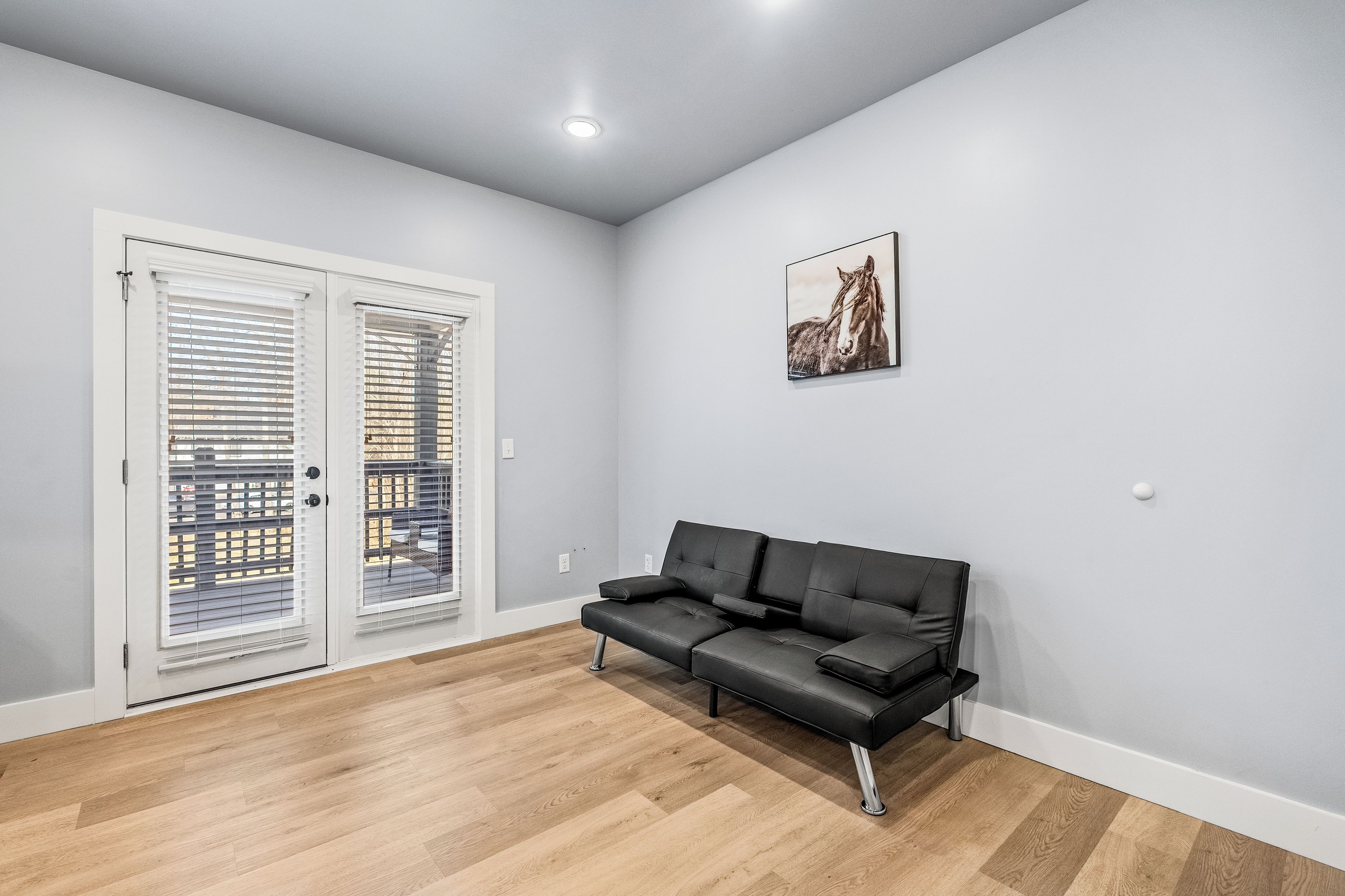 A room with a black leather sofa, a white door with blinds, and a ceiling light.