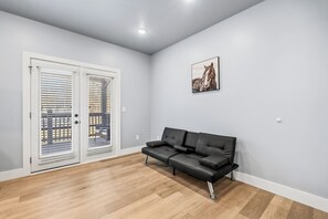 Una habitación con un sofá de cuero negro, una puerta blanca con persianas y una lámpara de techo.